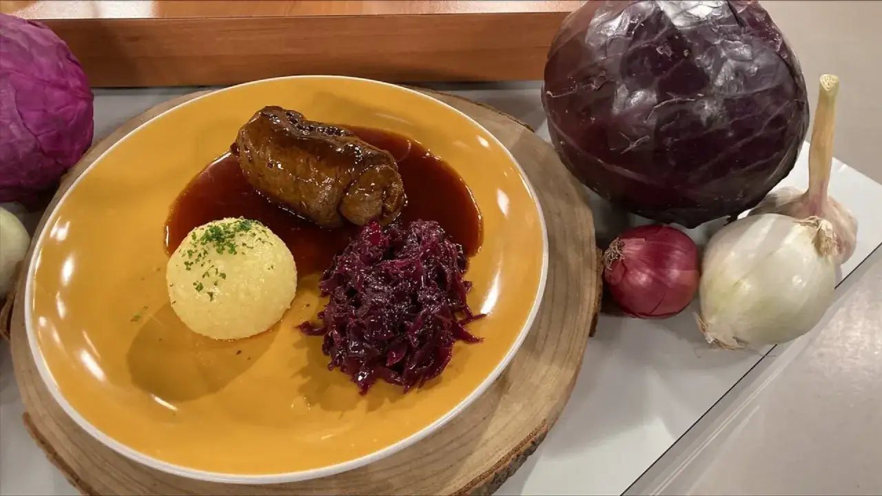 Herzhafte Roulade mit Klößen und Rotkohl – das passt perfekt zu Rouladen! Daneben liegen Zutaten für den Rotkohl: Rotkohl, Zwiebeln und Knoblauch.