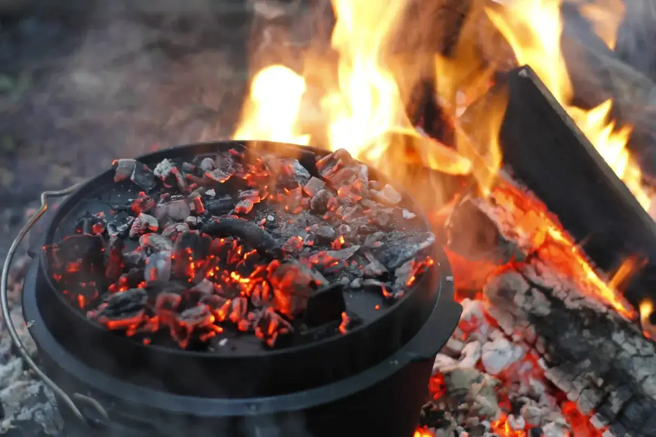 Glühende Kohlen auf einem Dutch Oven neben einem Lagerfeuer. Perfekt für spannende Dutch Oven Rezepte mit Kindern im Freien.