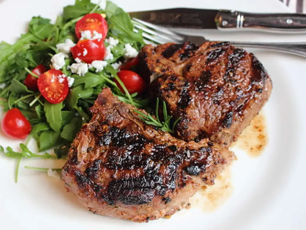 Zwei saftige Lammfilets, perfekt gegrillt, liegen neben einem frischen Rucolasalat mit Kirschtomaten und Feta. Ein Genuss für alle Sinne!