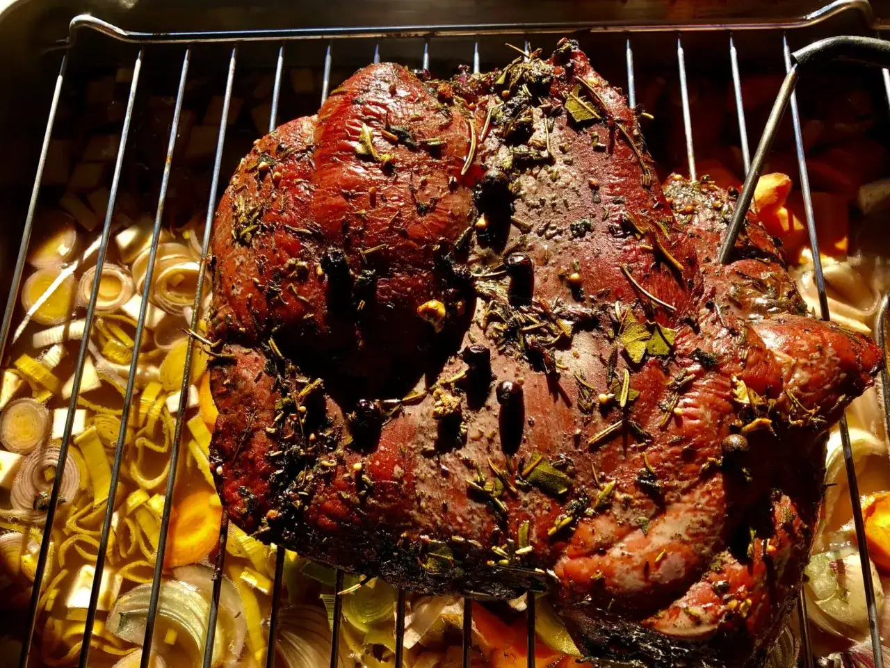 Ein saftiges Rehbraten mit Kr&auml;utern und Gew&uuml;rzen wird im Ofen gegrillt, umgeben von Wurzelgem&uuml;se.