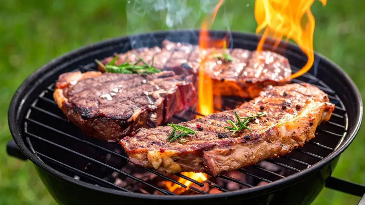 Saftige Rindersteaks mit Rosmarin und Pfeffer werden auf einem Grill mit Flammen zubereitet. Ein Genuss für jeden Grillmeister!