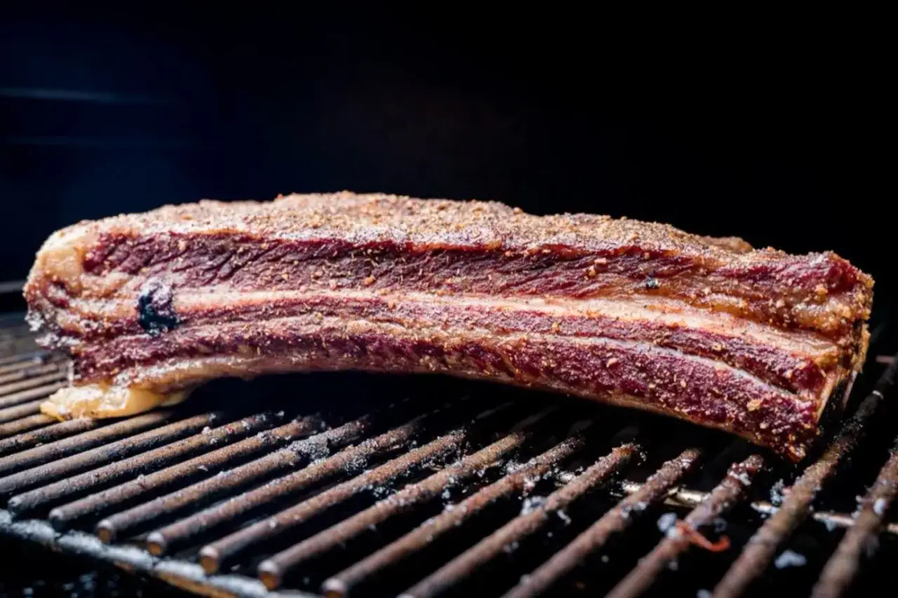 Ein saftiges Stück Rinderrippchen, gewürzt und auf einem Grillrost liegend, bereit für die Zubereitung.