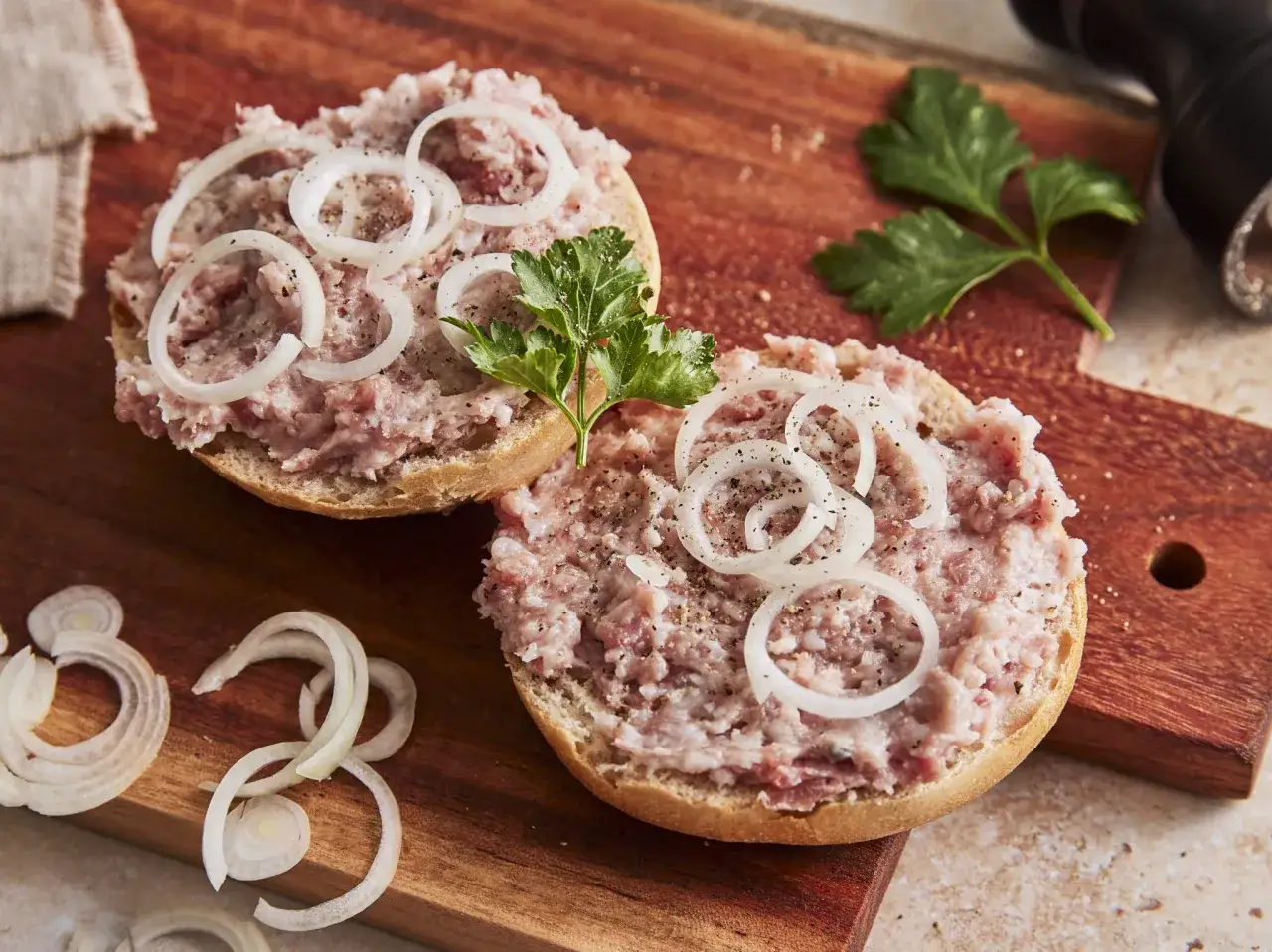 Zwei Brötchenhälften mit Mett, Zwiebelringen und Petersilie belegt. So sieht ein klassisches Mettbrötchen aus.