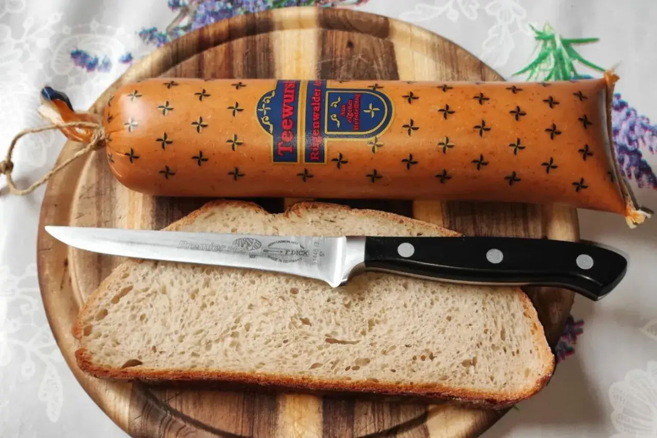 Teewurst, eine streichf&auml;hige Wurst, liegt auf Brot. Ein Messer liegt bereit, um die Teewurst zu schneiden.