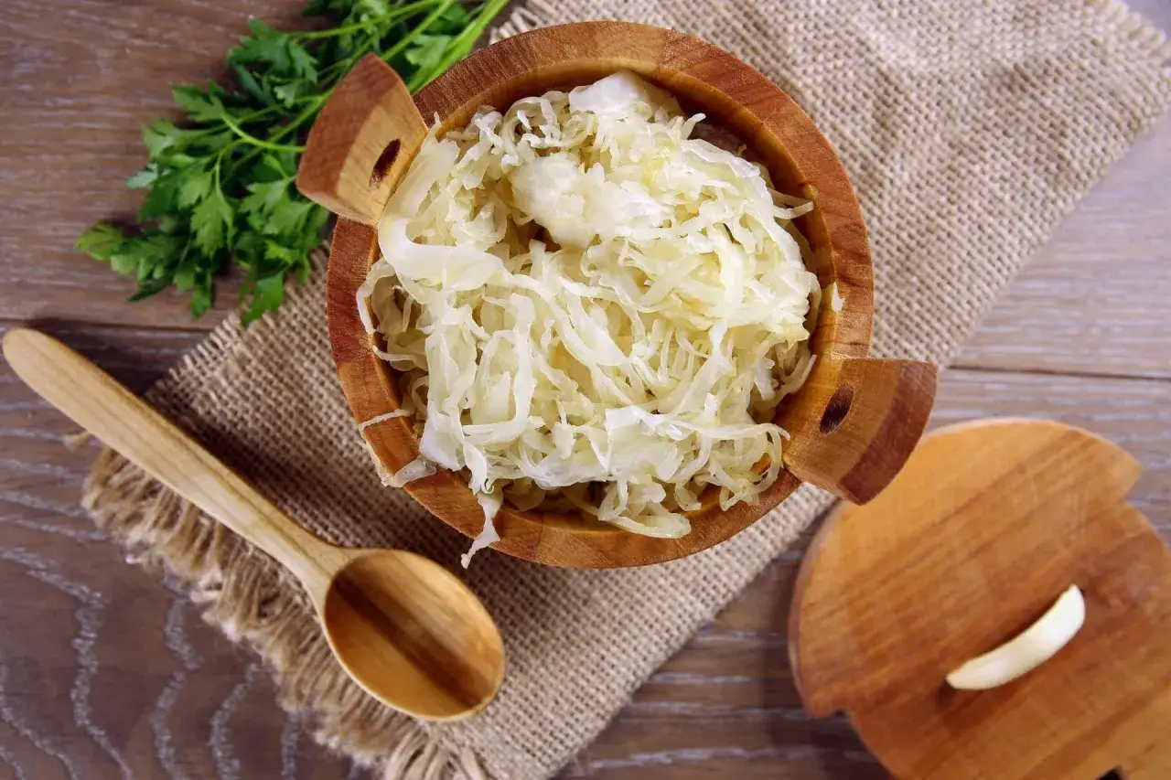 Holzschale mit Sauerkraut, daneben ein Holzlöffel und Petersilie. Perfekt für Ihr Sauerkraut Rezept!