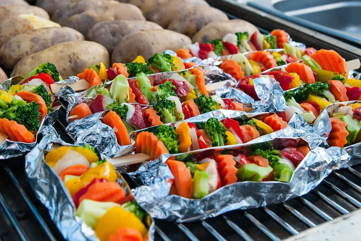 Bunte Gem&uuml;sespie&szlig;e in Alufolie auf dem Grill, daneben gebackene Kartoffeln. Perfekt f&uuml;r ein sommerliches BBQ.