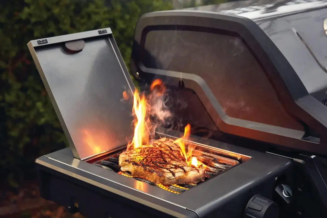 Ein saftiges Steak brutzelt in der Sizzle Zone eines Grills, umgeben von Flammen und Rauch.