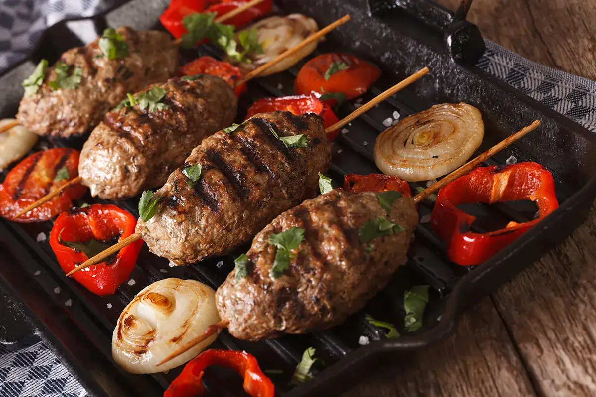 Saftige Bifteki vom Grill mit gegrilltem Gemüse wie Paprika und Zwiebeln, garniert mit frischer Petersilie.
