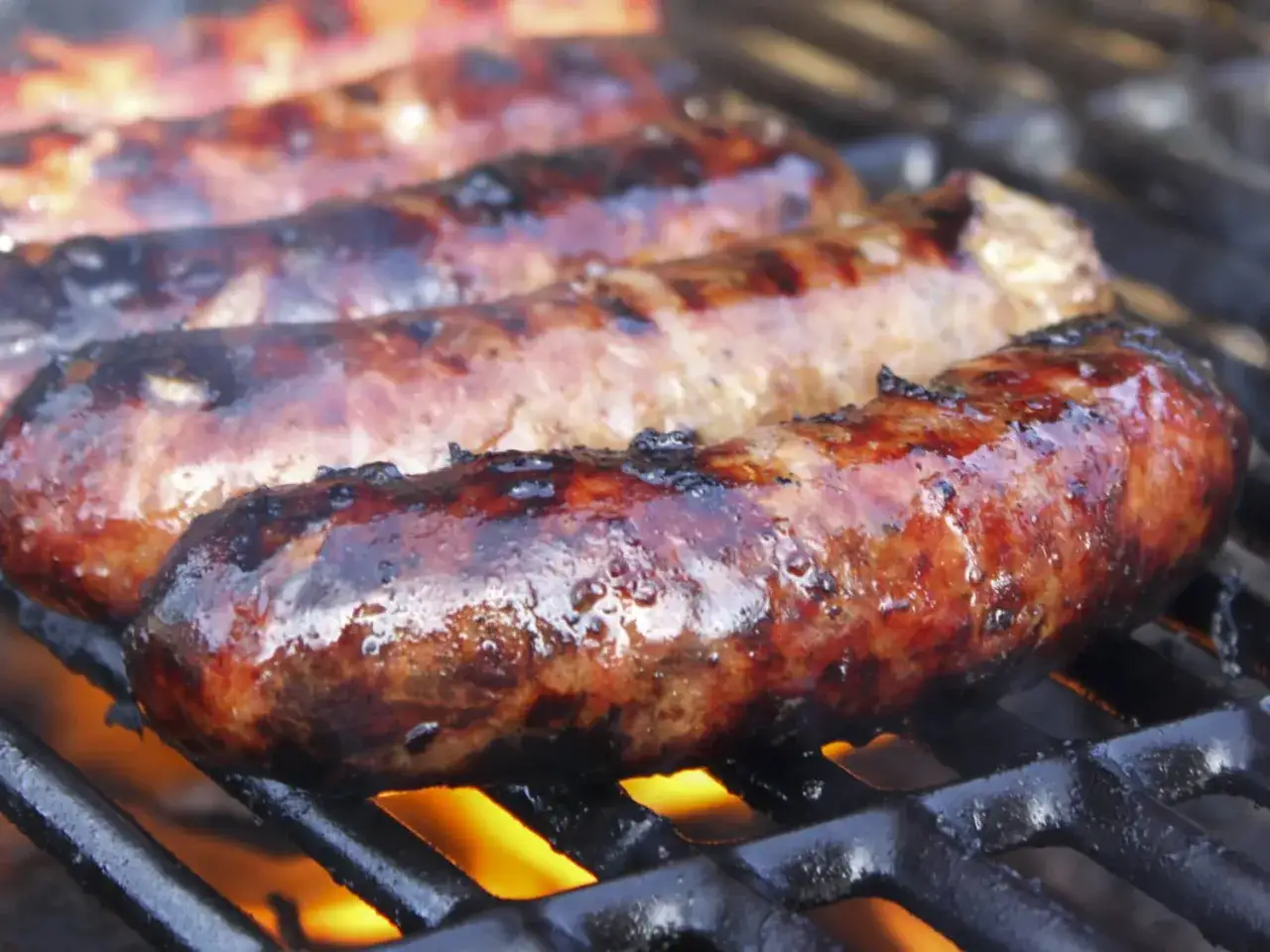 Saftige Salsiccia grillen über heißer Glut. Die Würste sind goldbraun und leicht angekohlt, bereit zum Genuss.