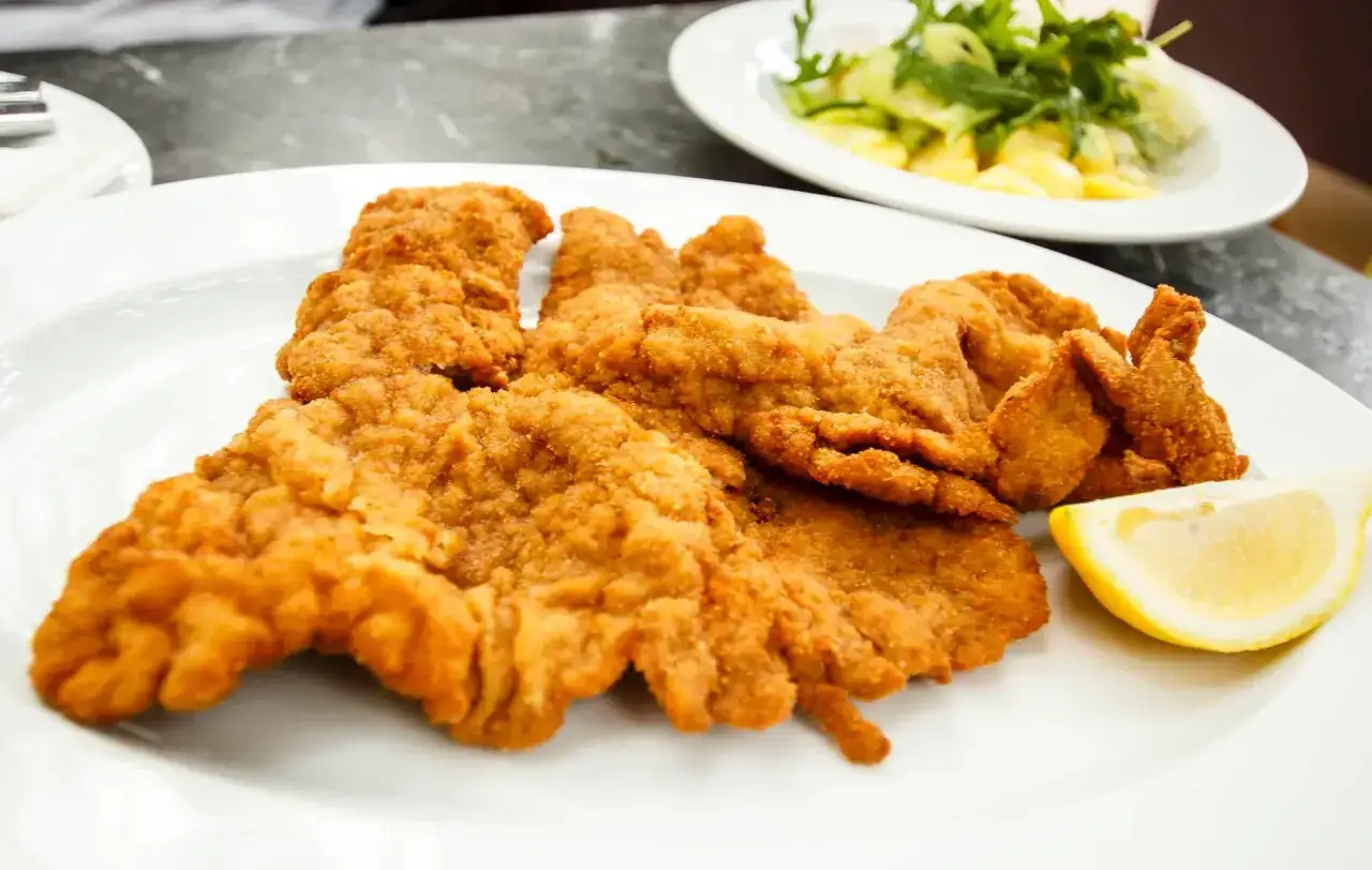 Goldbraunes Wiener Schnitzel, perfekt paniert, liegt auf einem Teller, daneben eine Zitronenspalte.