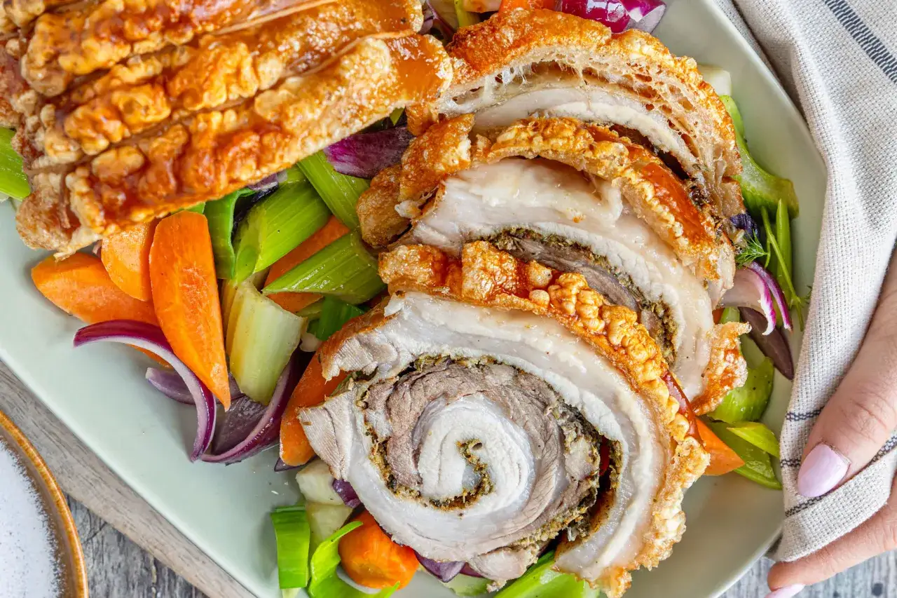 Saftiges porchetta rezept mit knuspriger Kruste, serviert mit karotten, sellerie und roten Zwiebeln.