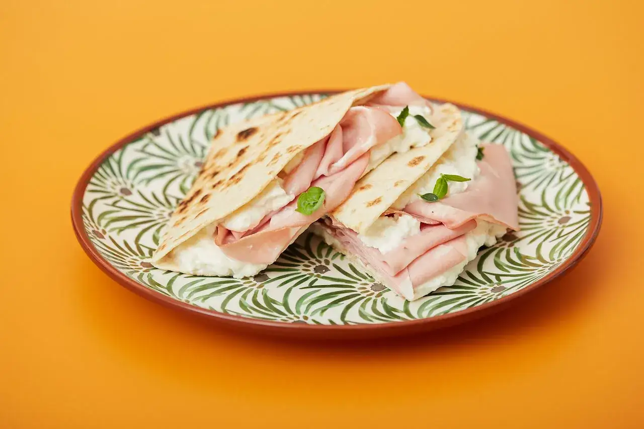 Piadina gefüllt mit cremigem Käse und zarter Mortadella, garniert mit Basilikum. Ein köstlicher Snack, der zeigt, was ist Mortadella.
