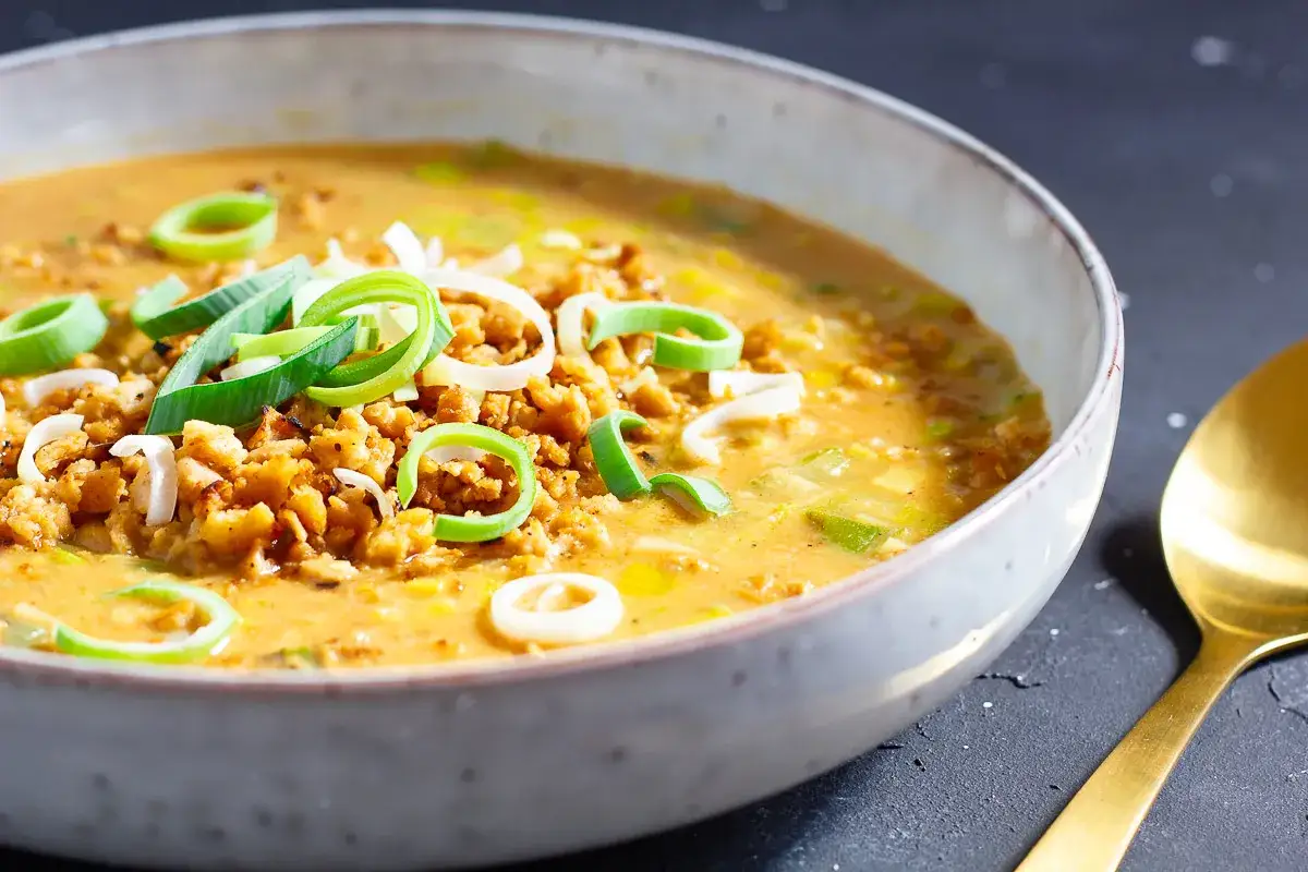Herzhafte hackfleisch lauch suppe in einer Schüssel, garniert mit frischem Lauch. Eine goldene Löffel liegt daneben.