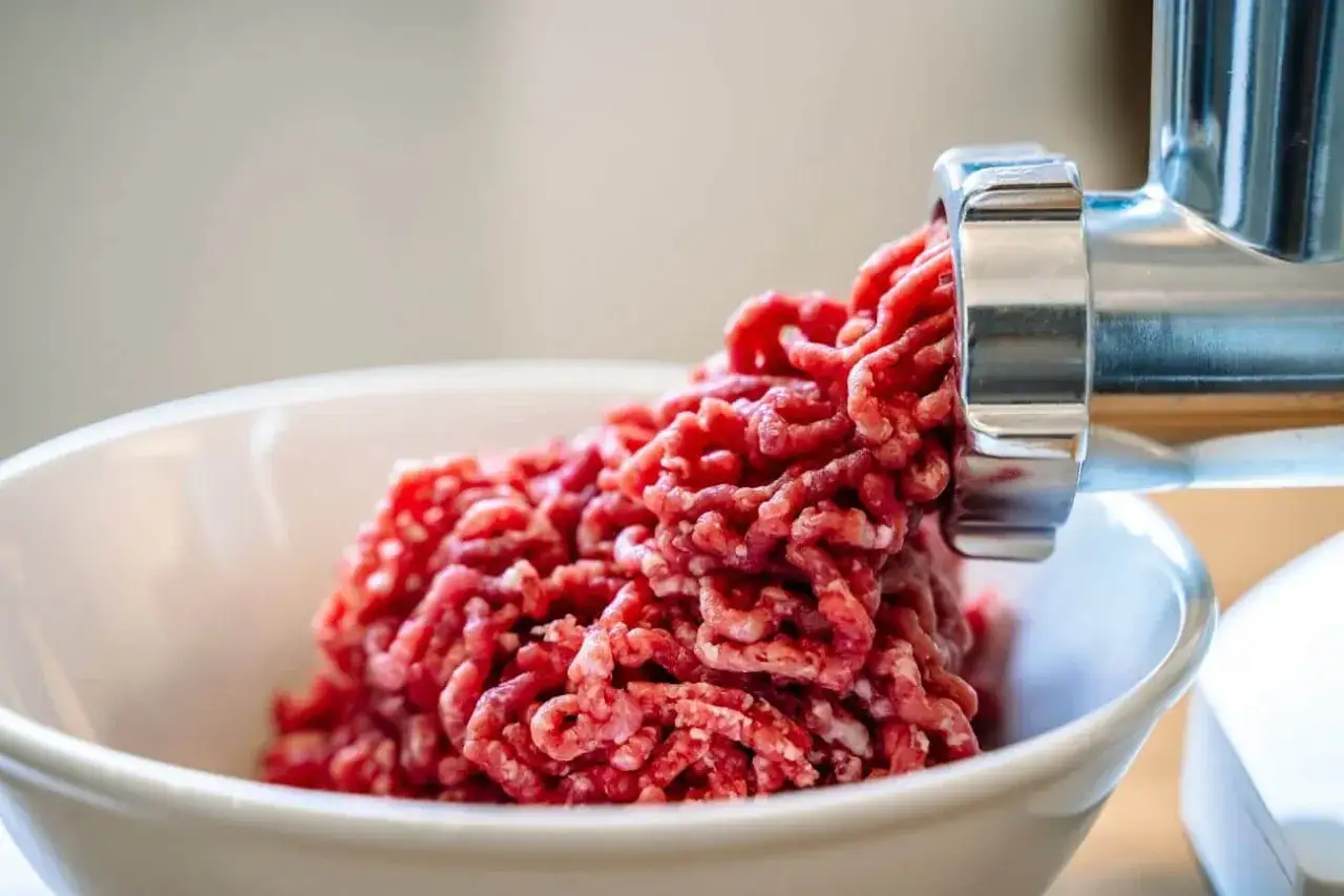 Frisch zubereitetes Hackfleisch fällt aus einer Fleischwolf-Schnecke in eine weiße Schüssel. So einfach ist es, Hackfleisch selber machen!