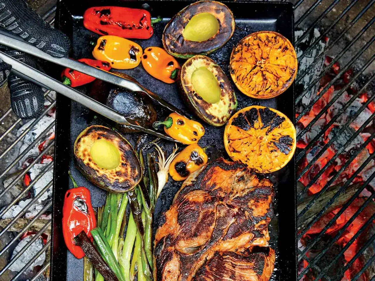 Fleisch, Avocados, Orangen und Paprika werden auf einer Plancha über glühender Kohle gegrillt.