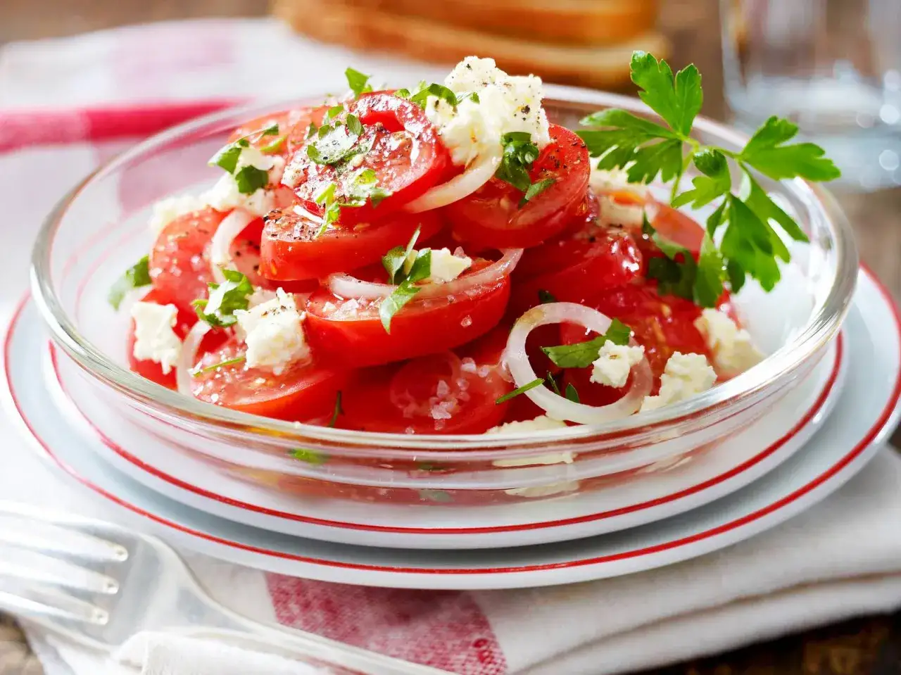 Frischer tomatensalat mit feta, Zwiebelringen und Petersilie, garniert mit schwarzem Pfeffer und Meersalz.