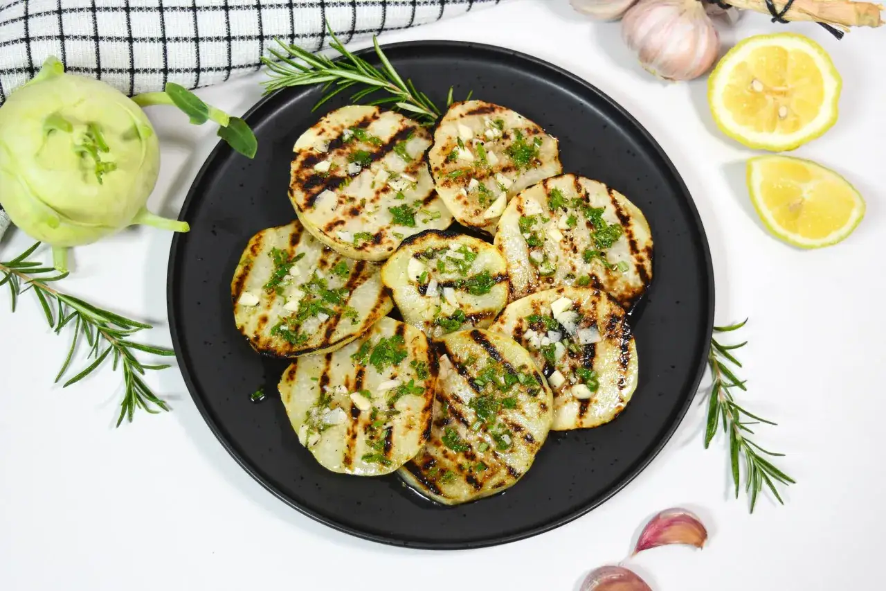 Gegrillte Kohlrabi-Scheiben mit Kräutern und Knoblauch, garniert mit Rosmarin. Dazu Zitronenspalten und frische Knoblauchzehen.