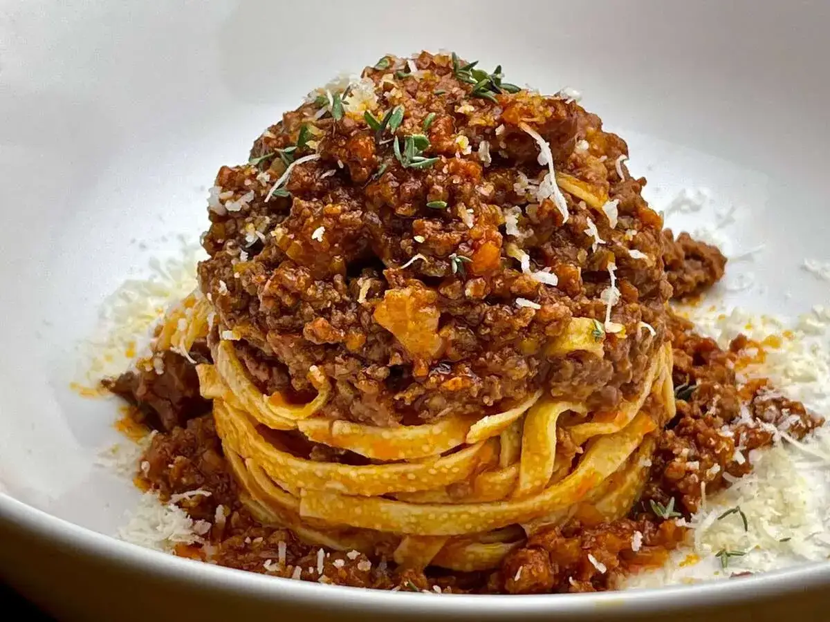 Ein Berg aus Tagliatelle, bedeckt mit einer herzhaften Bolognese-Sauce und garniert mit Parmesan und Kräutern. Ein Genuss für Augen und Gaumen.
