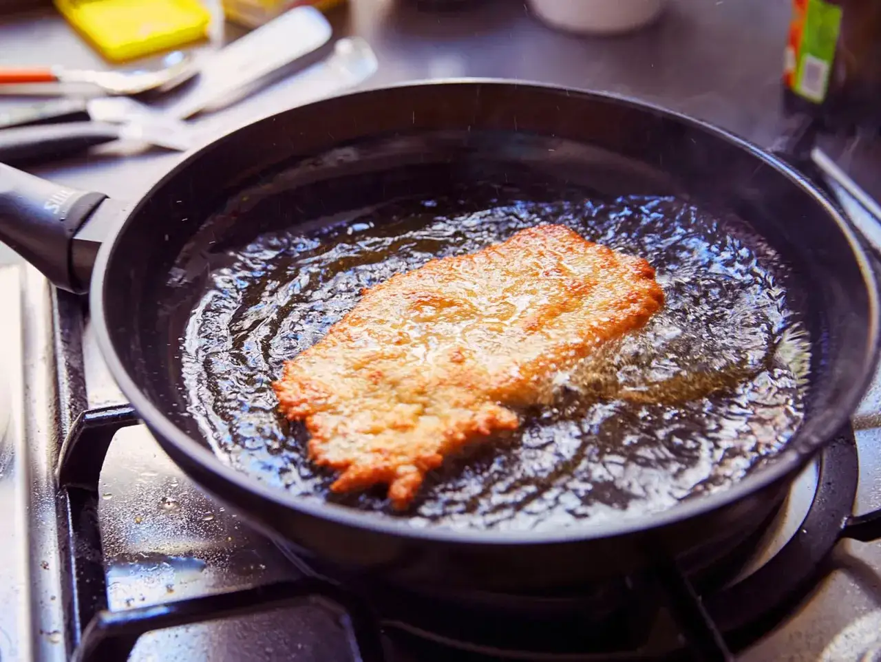 Ein goldbraunes Schnitzel braten in heißem Öl in einer Pfanne. Es zischt und dampft, während es perfekt zubereitet wird.