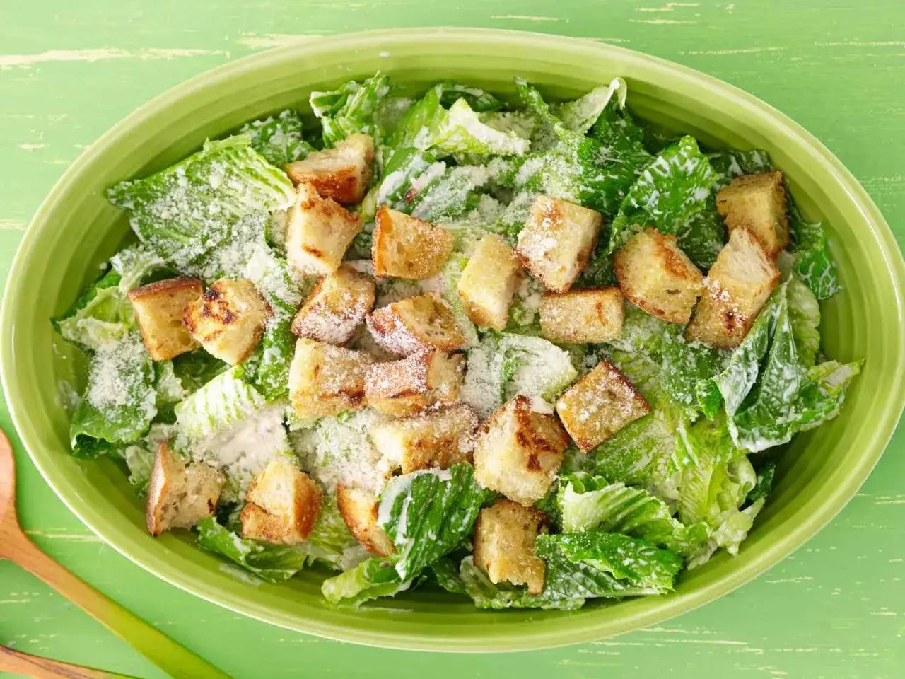 Frischer Caesar Salad mit knusprigen Croutons und Parmesan in einer grünen Schüssel.
