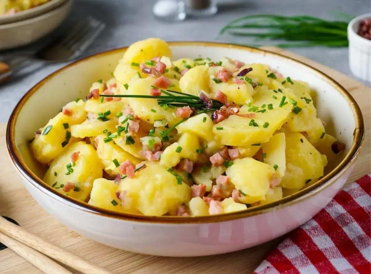 Schüssel mit warmem Kartoffelsalat, garniert mit Speckwürfeln und Schnittlauch. Ein Klassiker, der immer schmeckt!