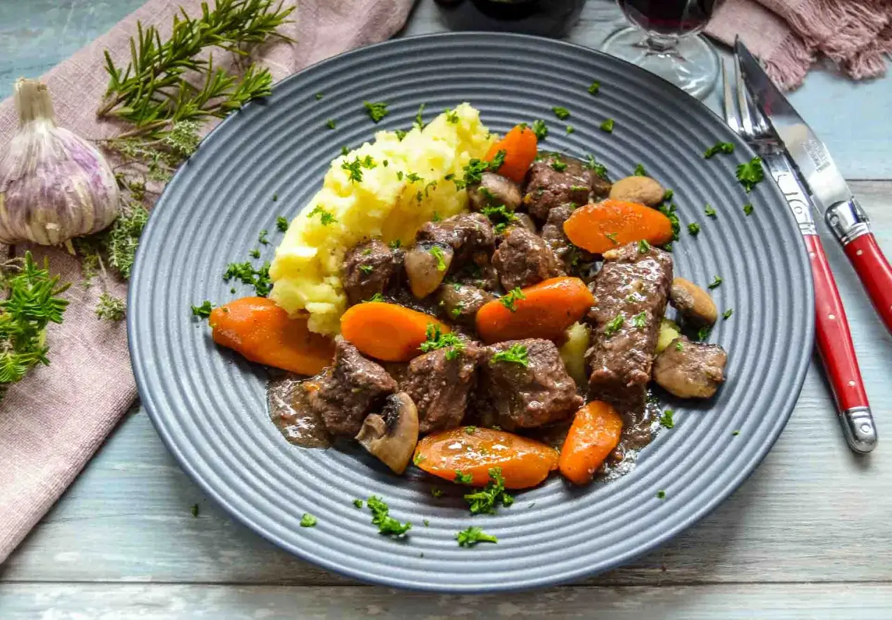 Herzhaftes Boeuf Bourguignon mit Kartoffelpüree, Karotten und Pilzen, garniert mit Petersilie.