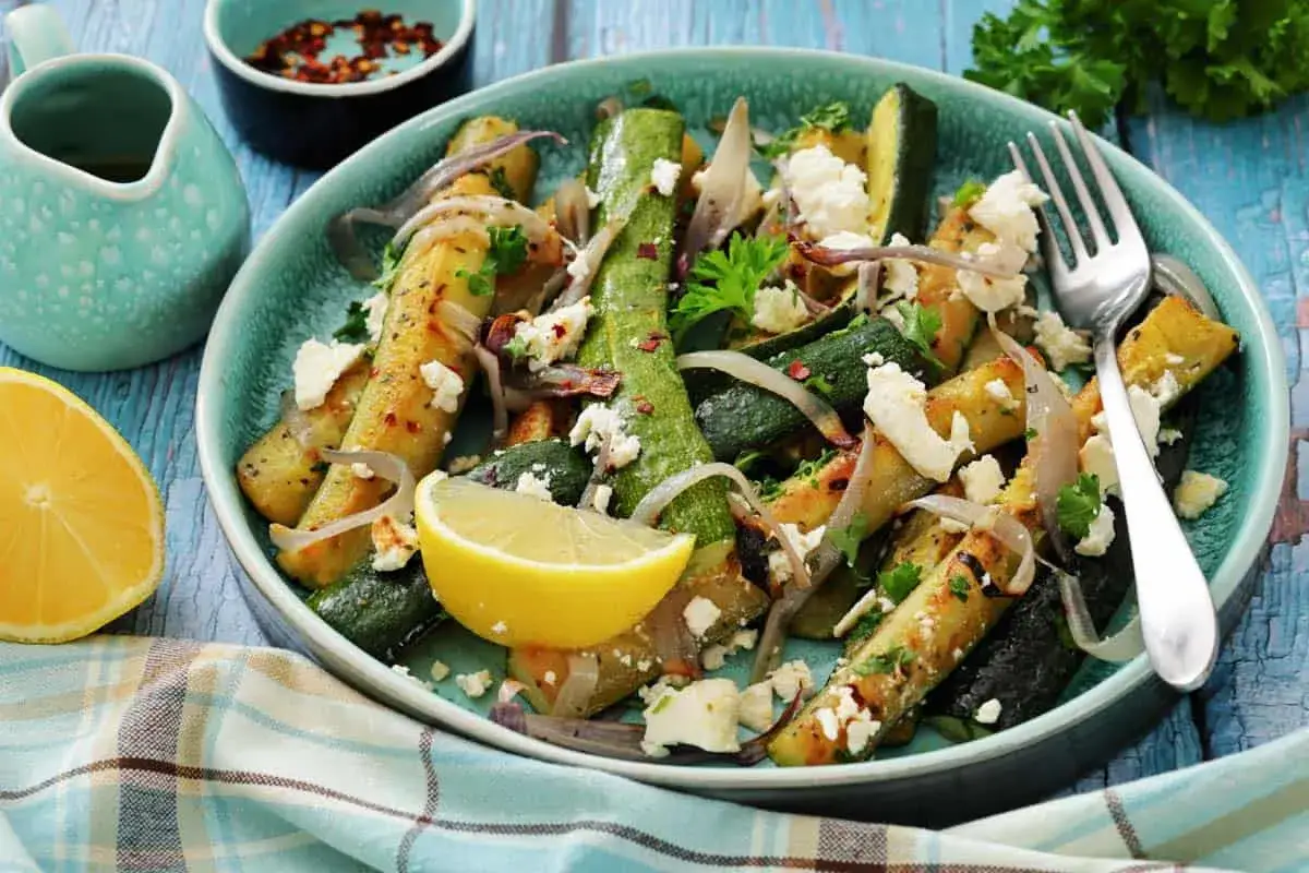 Gegrillte Zucchini mit Feta, Zwiebeln und Zitrone auf einem t&uuml;rkisfarbenen Teller. Ein k&ouml;stliches Gericht, perfekt f&uuml;r den Sommer.