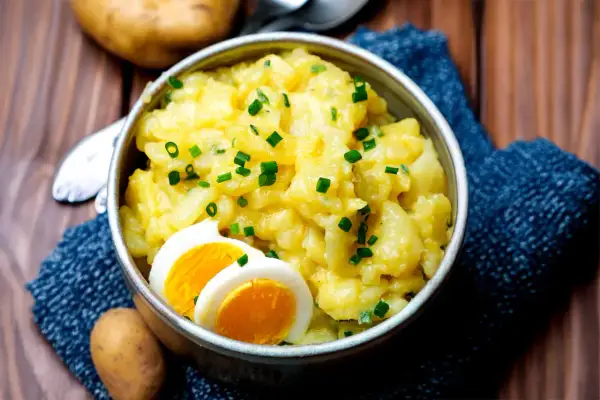 Schüssel mit warmem Kartoffelsalat, garniert mit Schnittlauch und Ei. Ein Klassiker, der immer schmeckt.