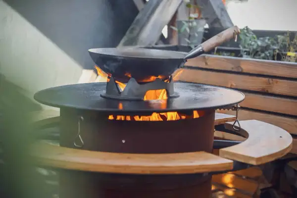 Ein Wok auf einem Feuerring, der an eine Plancha erinnert, wird draußen erhitzt.