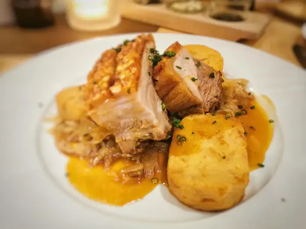 Saftiger Schweinebraten Niedrigtemperatur mit knuspriger Kruste, Kartoffelklößen und dunkler Soße auf einem weißen Teller.