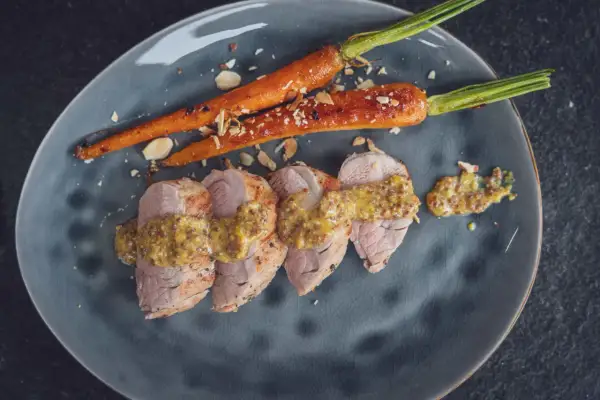 Zarte Scheiben von **schweinefilet grillen** mit Honig-Senf-Sauce und karamellisierten Karotten, bestreut mit Mandelsplittern.