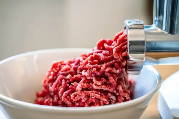 Frisches Hackfleisch wird aus einem Fleischwolf in eine Schüssel gedrückt. So kann man Hackfleisch selber machen.