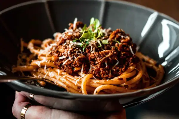Eine Schüssel mit köstlichen Spaghetti Bolognese, garniert mit frischen Kräutern und geriebenem Parmesan.