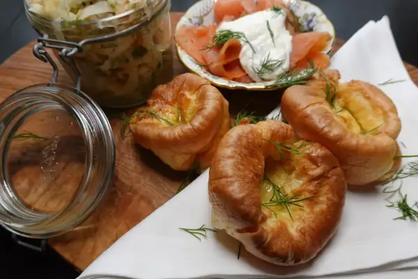 Goldbraune Yorkshire Pudding-Törtchen mit Dill garniert, daneben Lachs mit Frischkäse und ein Glas Sauerkraut.