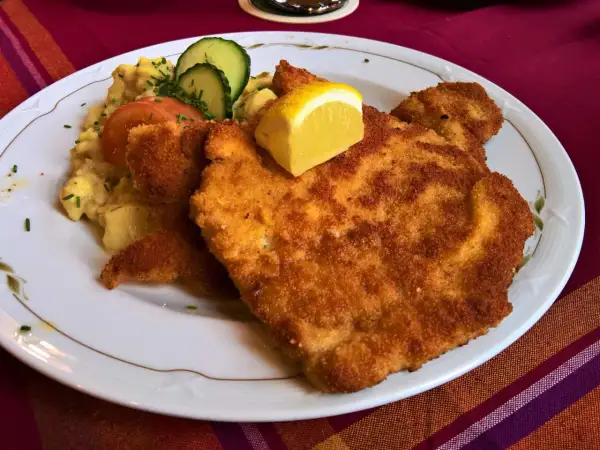 Perfekt paniertes Wiener Schnitzel mit Kartoffelsalat, Tomate, Gurke und Zitrone. Ein Genuss, der zeigt, wie gut Wiener Schnitzel panieren gelingt.