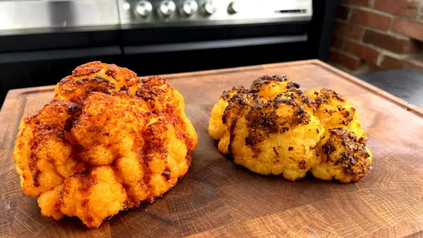 Zwei perfekt gegrillte Blumenkohlröschen liegen auf einem Holzbrett. Sie sind goldbraun und leicht angekohlt, was auf köstliches blumenkohl grillen hindeutet.