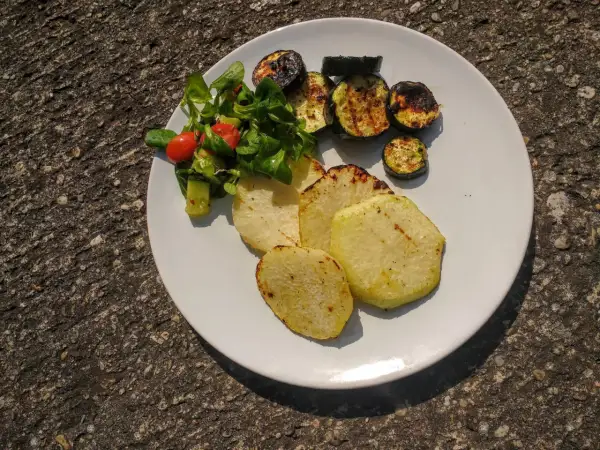 Gegrillte Kohlrabi-Scheiben mit Zucchini und einem kleinen Salat auf einem weißen Teller. Ein leckeres Sommergericht!