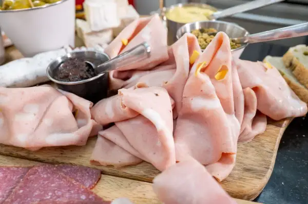 Dünn geschnittene Mortadella, eine italienische Brühwurst, liegt auf einem Holzbrett neben Salami und Oliven.