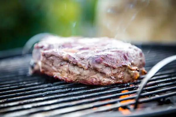 Ein saftiges Rindersteak grillen, Rauch steigt auf, die Flammen lodern darunter. Perfekt für den Grillabend!