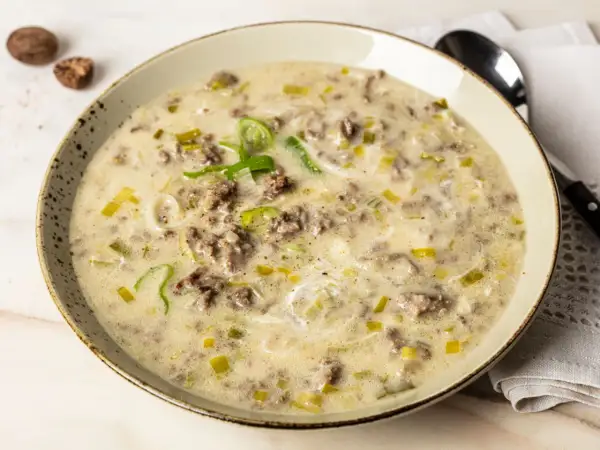 Eine cremige hackfleisch lauch suppe, garniert mit frischem Lauch und Gewürzen, serviert in einer rustikalen Schüssel.