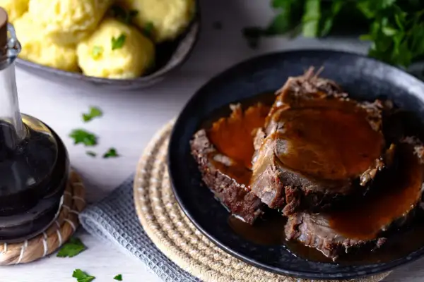 Zartes Fleisch in dunkler Sauce, perfekt für ein klassisches Sauerbraten Rezept. Dazu Klöße und frische Petersilie.