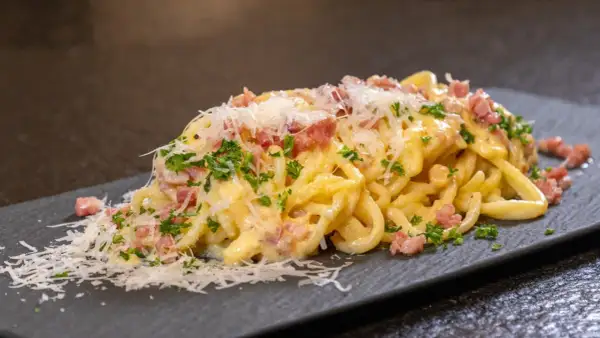 Ein Teller cremiger Spaghetti Carbonara, garniert mit Speckwürfeln, Petersilie und frisch geriebenem Parmesan.