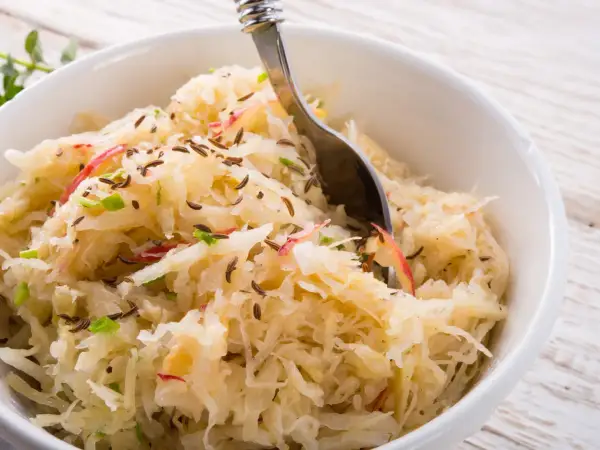 Schüssel mit Sauerkraut, verfeinert mit Kümmel und Apfelstücken. Eine Gabel ragt hinein, bereit zum Genießen.