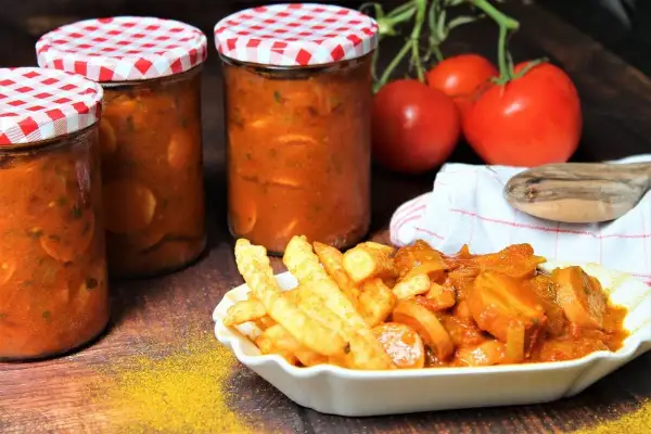 Gläser mit Currywurst-Sauce zum Einkochen, daneben eine Portion Currywurst mit Pommes.