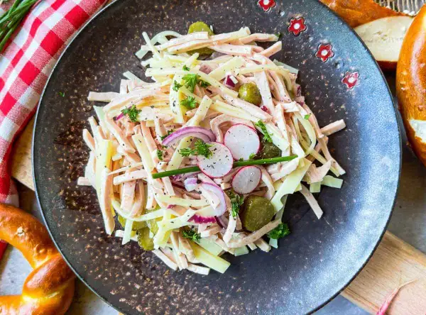 Ein herzhafter schweizer wurstsalat mit Käse, Radieschen, Gurken und Zwiebeln, garniert mit Petersilie.