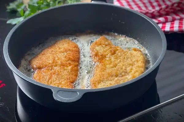 Zwei panierte Schnitzel braten in heißem Öl. Die goldbraune Kruste verspricht ein perfektes Ergebnis.