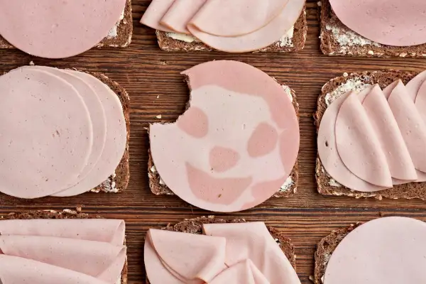 Biss in Lyoner: Welche Wurst ist gesund? Mehrere Brotscheiben mit Wurst belegt, liegen auf Holzuntergrund.
