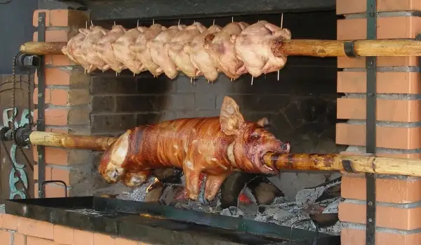 Ein Spanferkel grillen über offenem Feuer. Darüber hängen mehrere Hähnchen am Spieß.