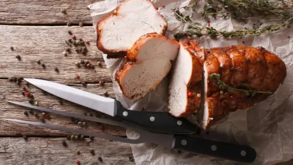 Saftiges braten fleisch, aufgeschnitten, mit Kräutern und Pfefferkörnern auf Holz. Messer und Fleischgabel liegen bereit.