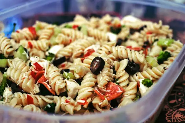 Ausgefallene Salate zum Grillen schnell gemacht: Nudelsalat mit Spiralnudeln, Oliven, Paprika und Brokkoli in einer Plastikschüssel.